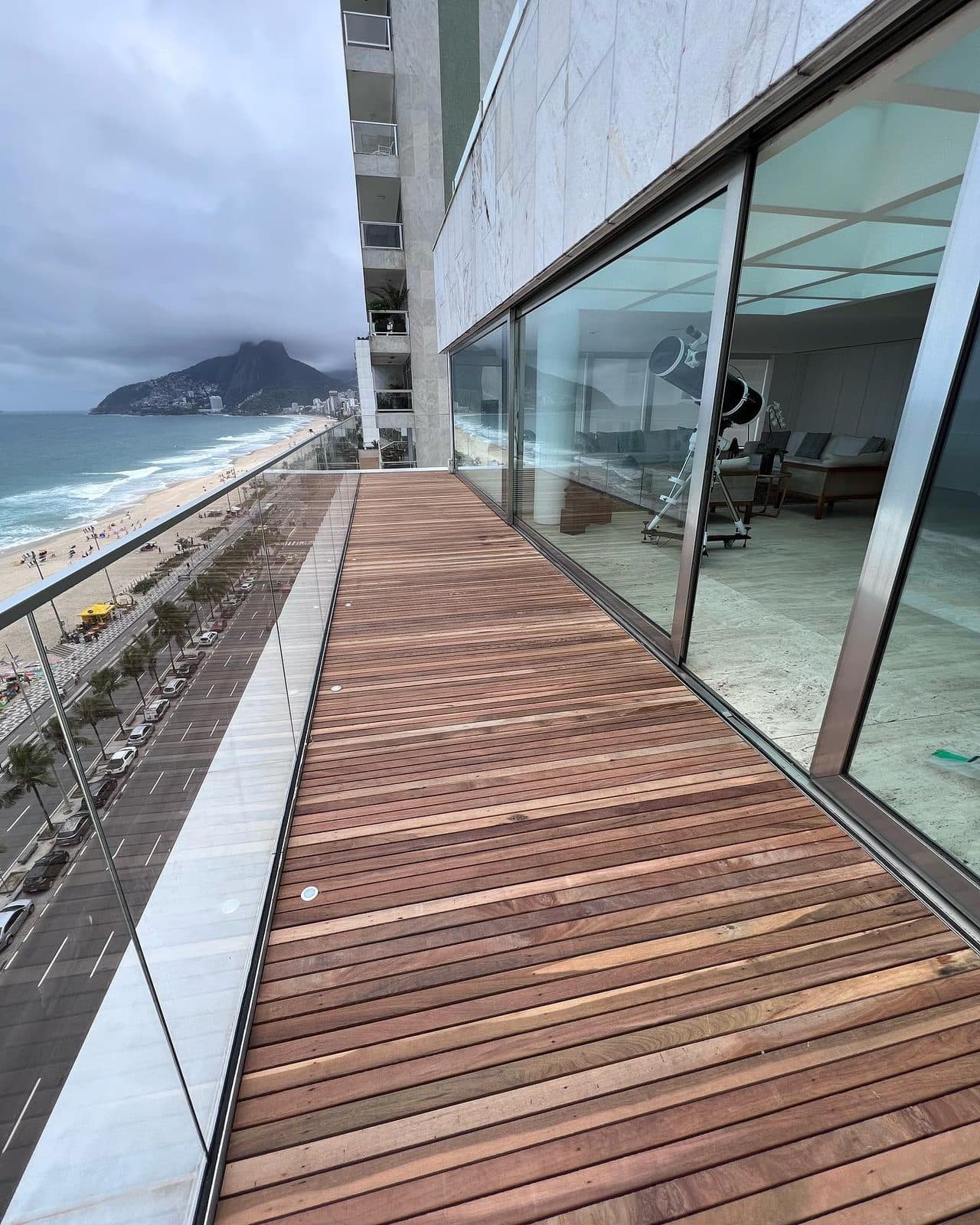 Deck ripado alinhado à fachada de vidro, vista da praia