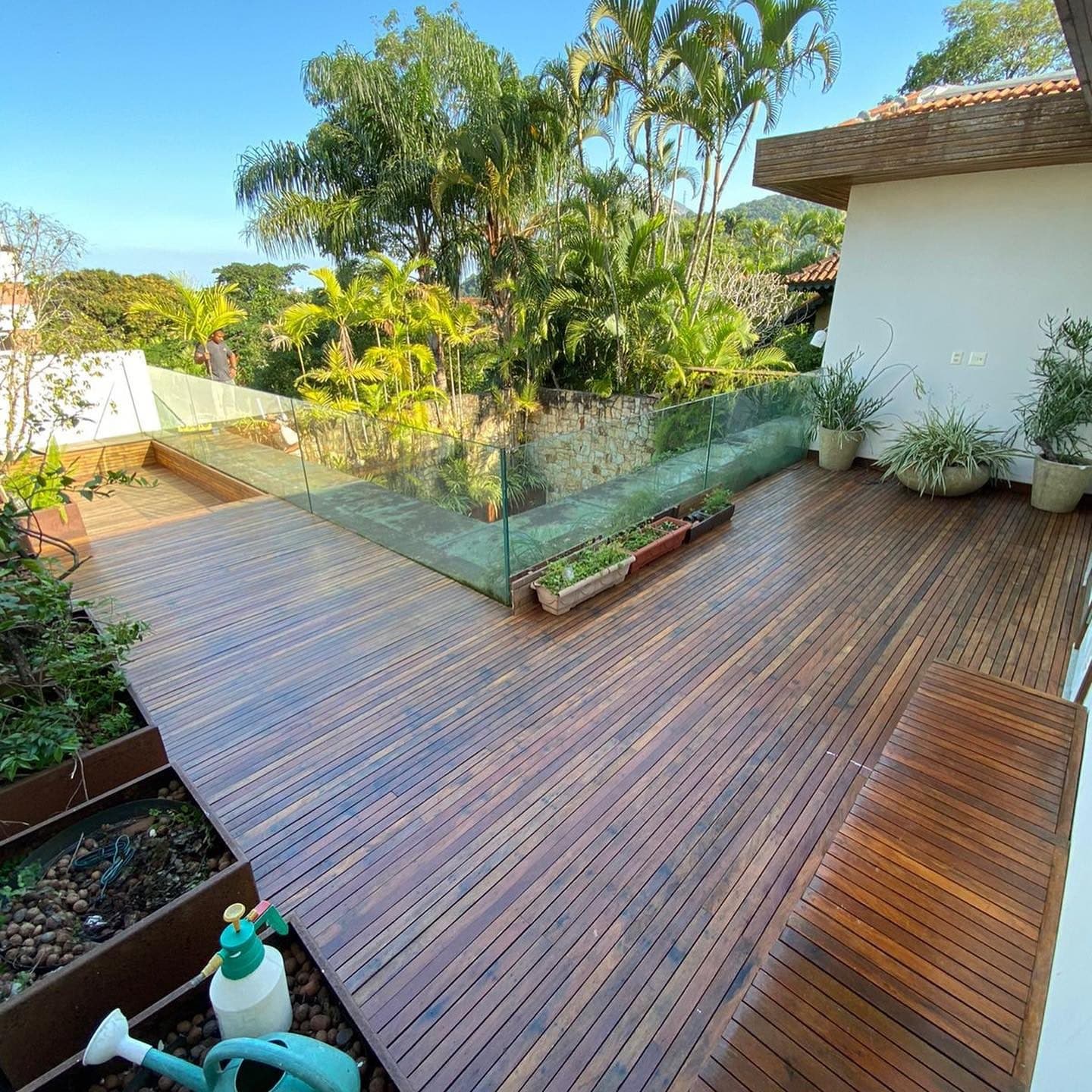 Deck de ipê em L com guarda-corpo de vidro e jardim tropical