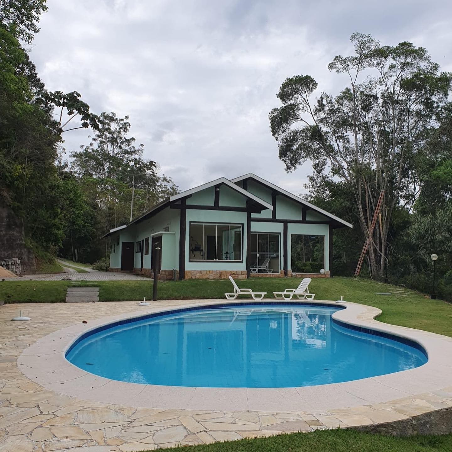 Casa branca com estrutura de madeira escura, piscina e gramado