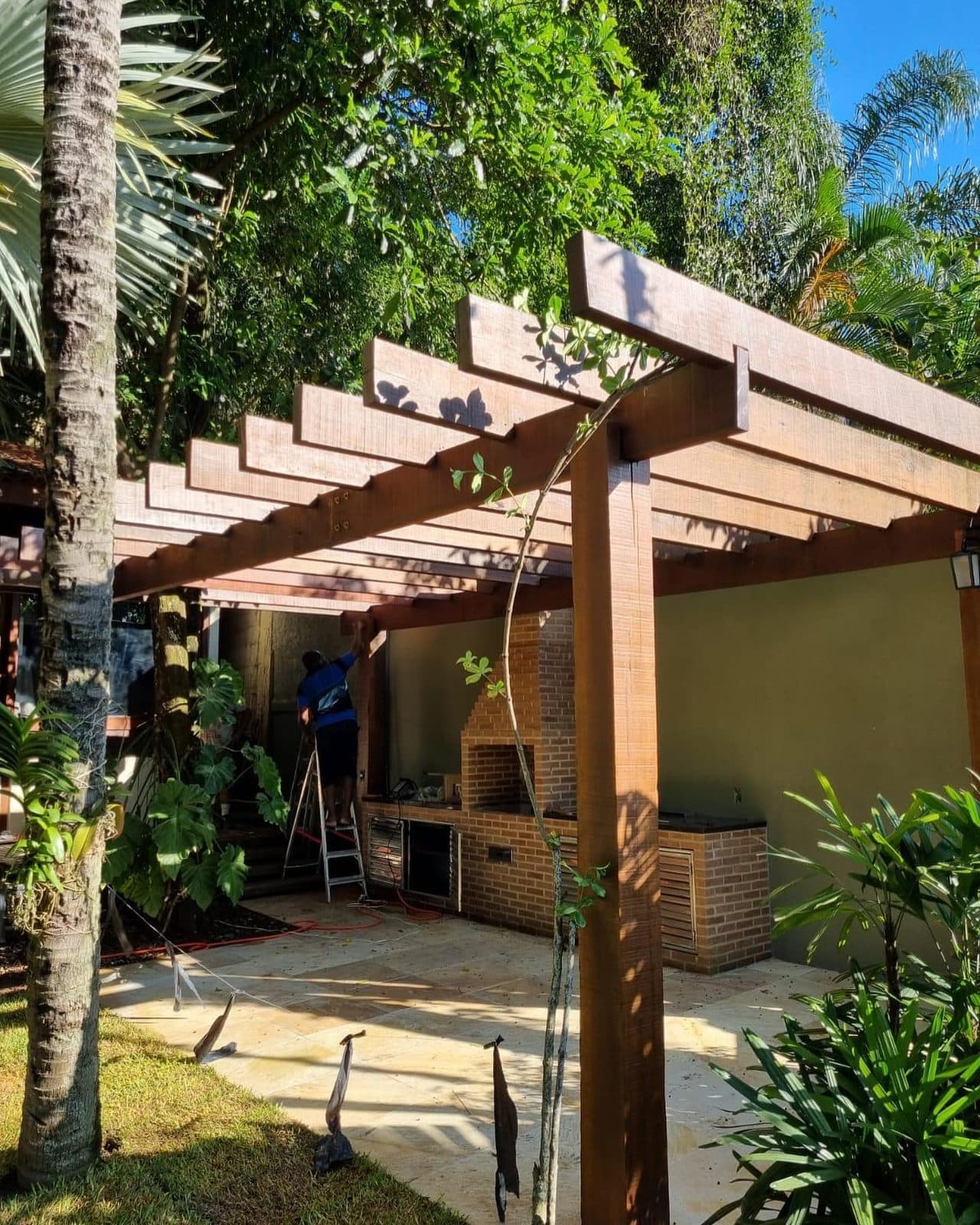 Pergolado de massaranduba sobre área gourmet em jardim tropical
