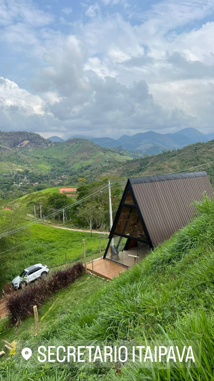 A-frame de telhado metálico em encosta verde, serra ao fundo