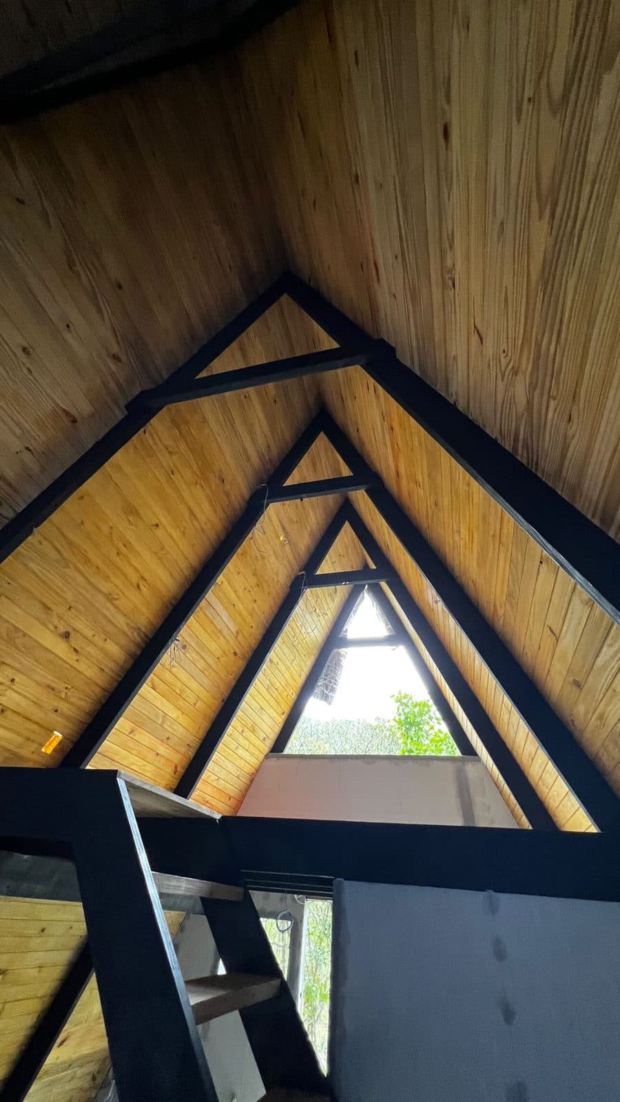 Teto interno de chalé A-frame com tesouras pretas e forro de pinus