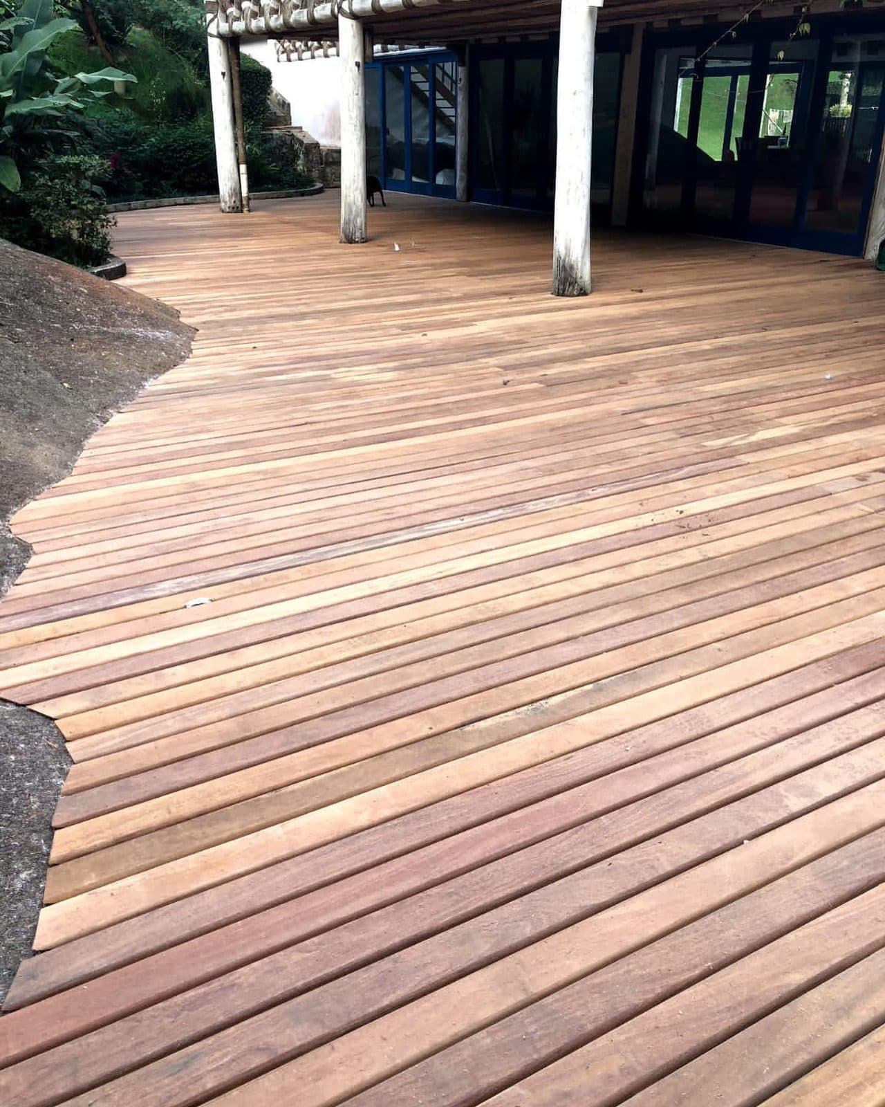 Deck de cumaru contornando rocha, casa com pilares brancos ao fundo