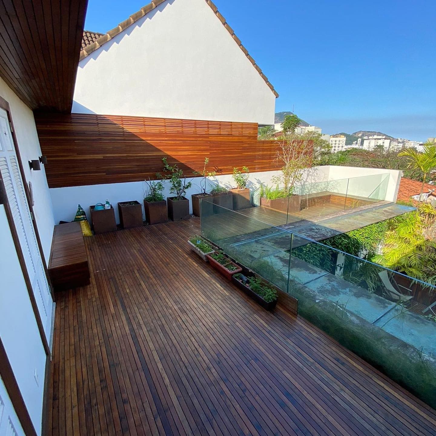 Deck ripado de ipê em terraço com guarda-corpo de vidro e jardineiras