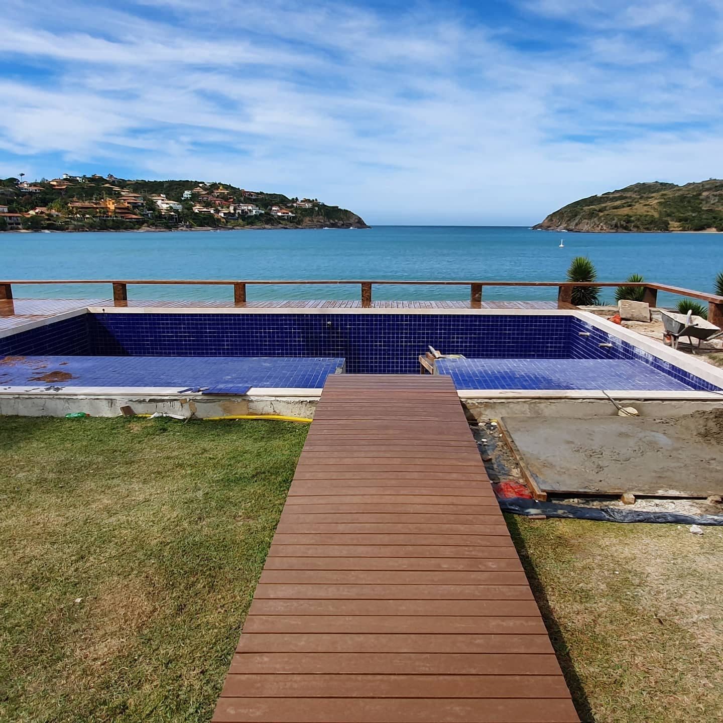 Passarela de deck cruzando o gramado até a piscina de borda infinita e o mar