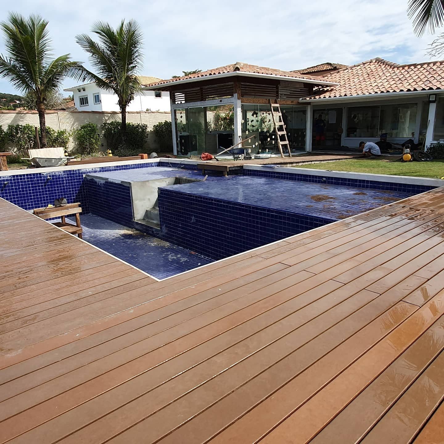Deck de madeira plástica contornando a piscina, casa de praia ao fundo