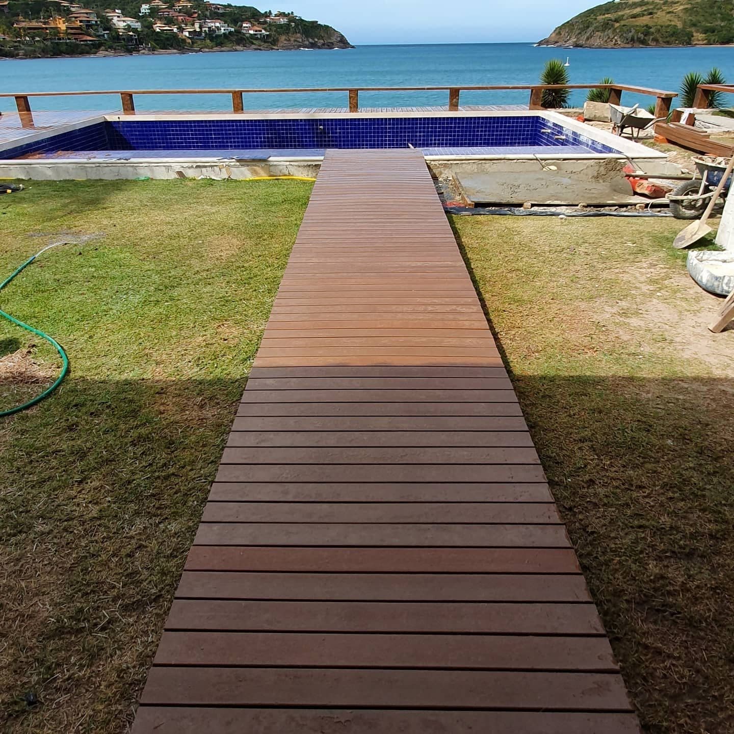 Passarela longa de deck, gramado, piscina e mar ao fundo