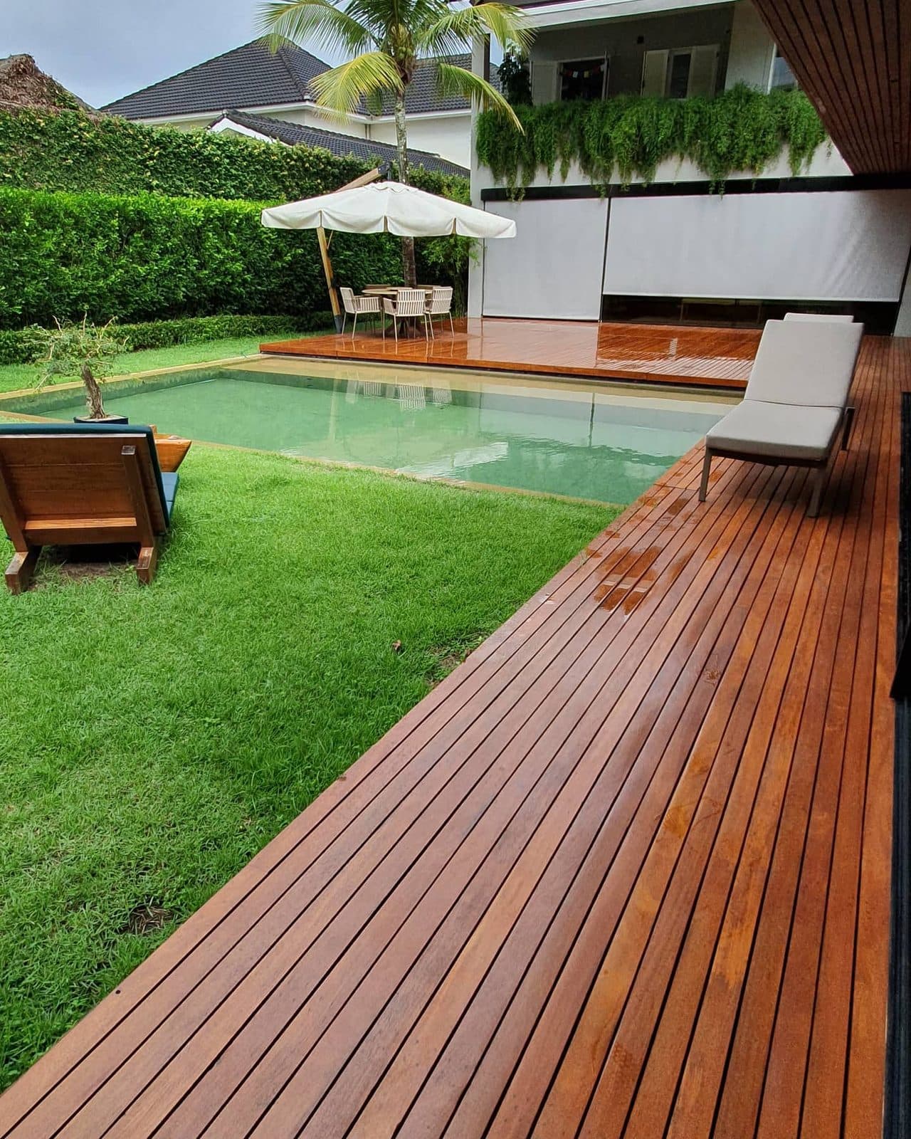 Deck de madeira natural junto à piscina com gramado e espreguiçadeiras