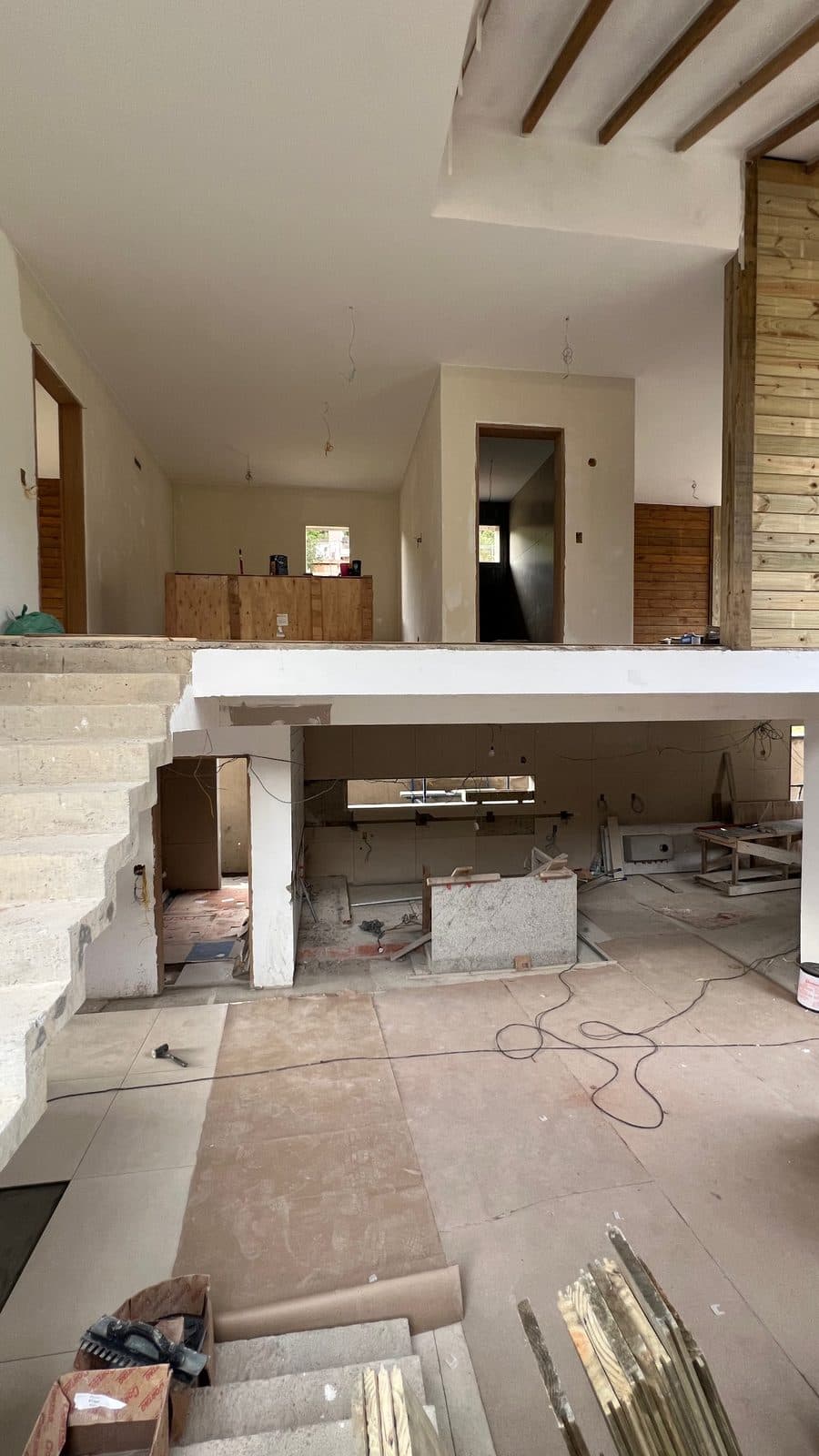 Pé-direito duplo em obra: escada de concreto, bancada e parede de madeira
