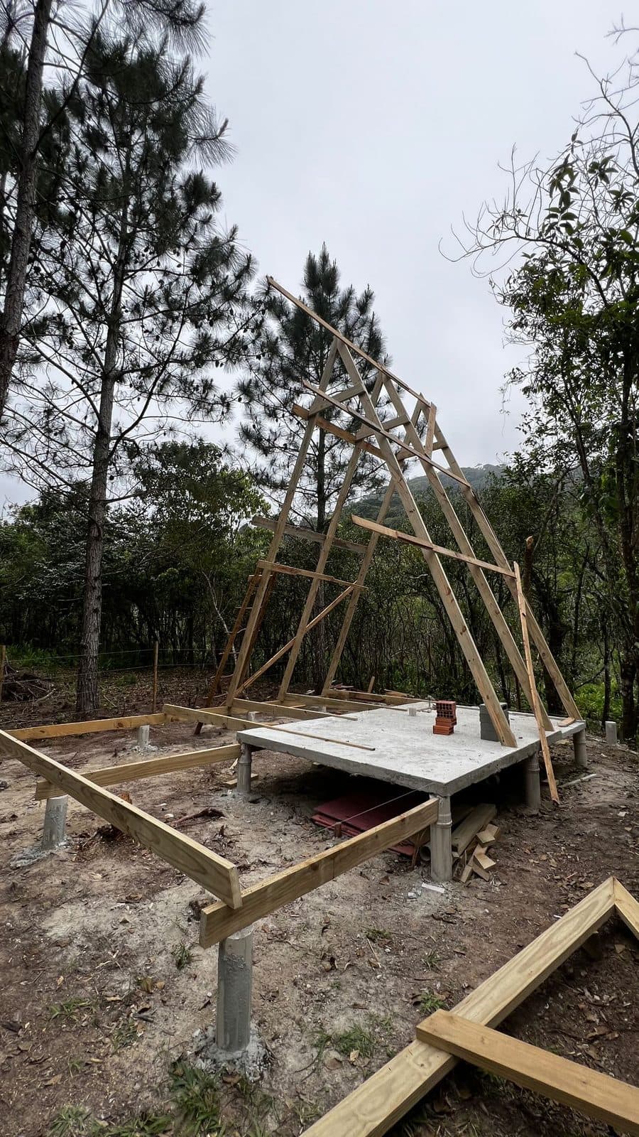 Esqueleto de chalé A-frame em madeira sobre base de concreto na mata