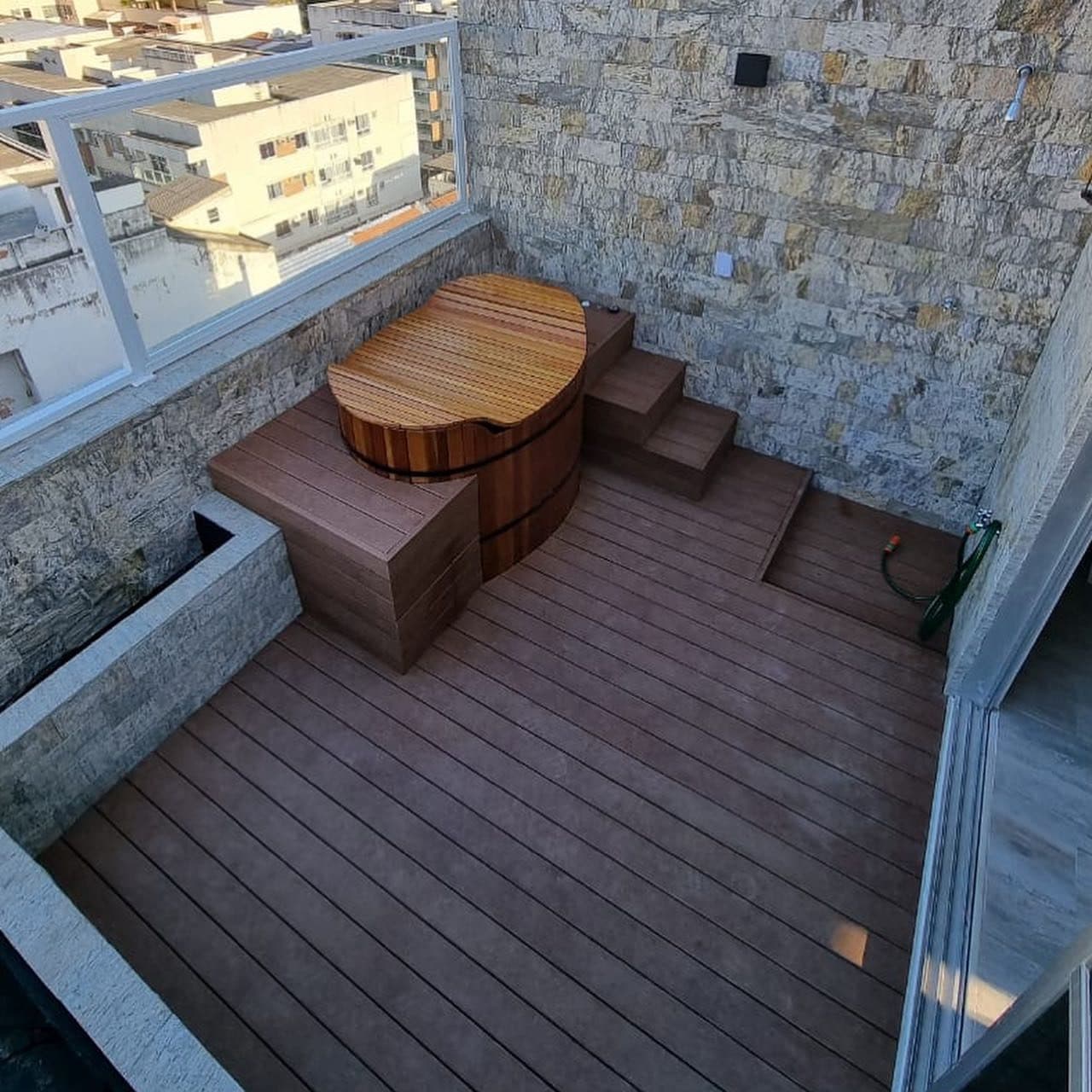 Ofurô de madeira e deck de madeira plástica em varanda com pedra
